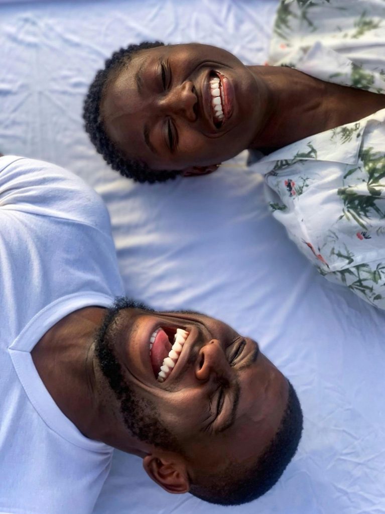 Two friends sharing laughter while lying on a sunny outdoor setting in Abuja, Nigeria.